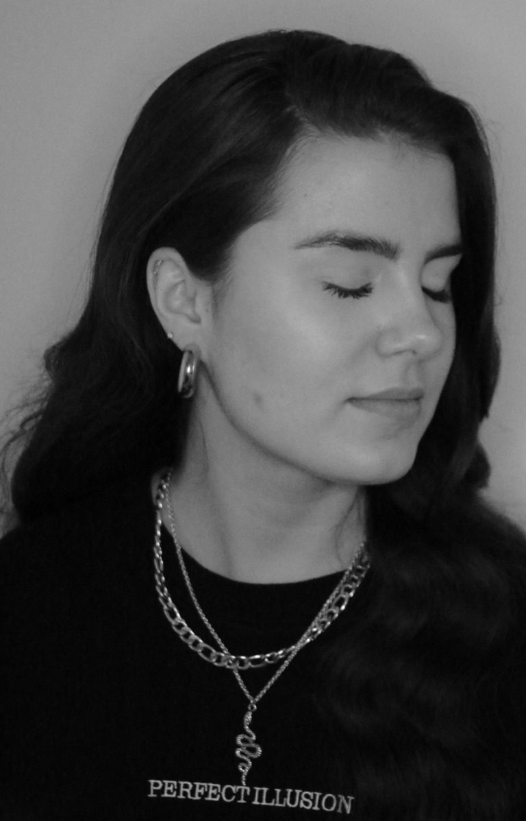 Porträt von LIIVIA mit geschlossenen Augen und gewelltem Haar, schwarze Kleidung und Schmuck.